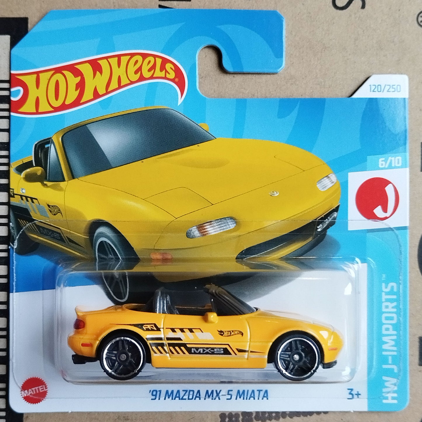 Hot Wheels J-Imports HW J-Imports '91 Mazda MX-5 Miata toy car in its original blister card packaging, featuring a bright yellow convertible with black and gray racing decals.