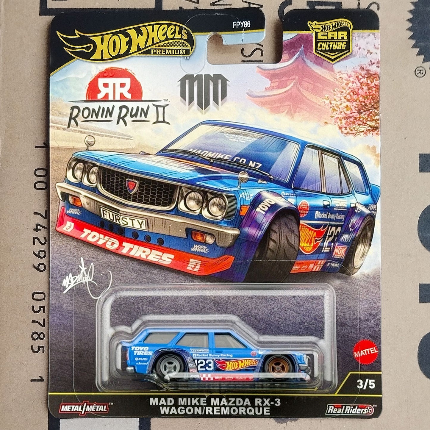Hot Wheels Mattel Real Riders Ronin Run II Mad Mike Mazda RX-3 Wagon/Remorque die-cast model car in its original blister packaging, featuring a blue and purple Mazda RX-3 with racing decals.