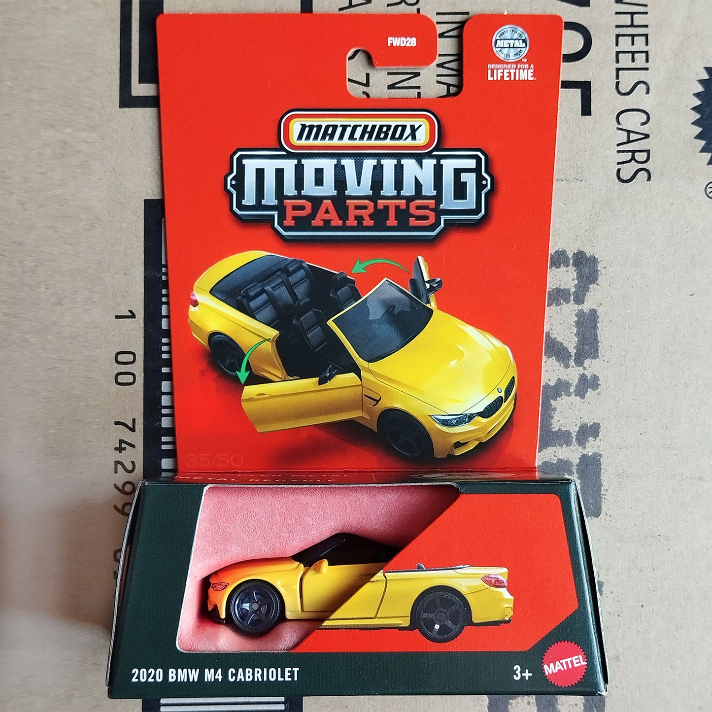 Matchbox Moving Parts 2020 BMW M4 Cabriolet die-cast toy car in its original red and black packaging, displayed on top of a cardboard shipping box.