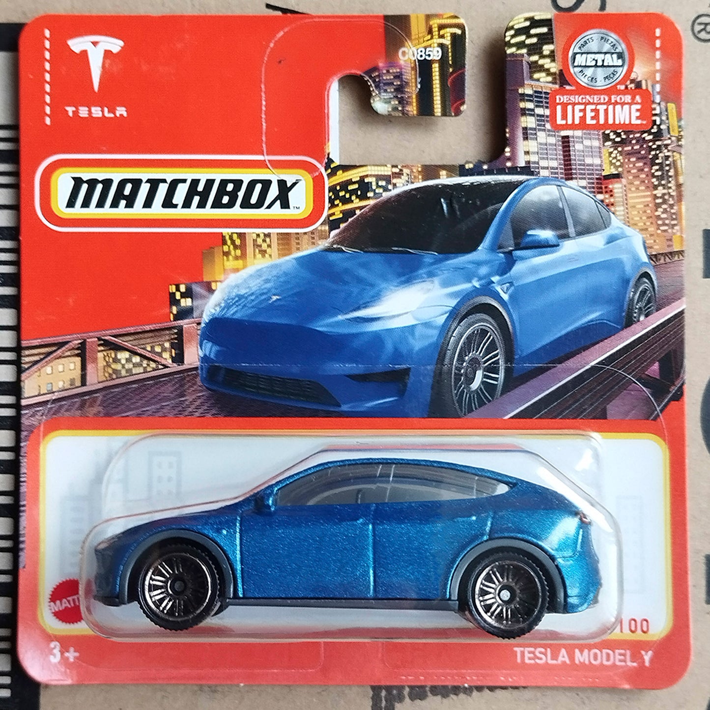 A Matchbox toy car in its original blister packaging, featuring a metallic blue Tesla Model Y die-cast model car on a red and orange backing card.